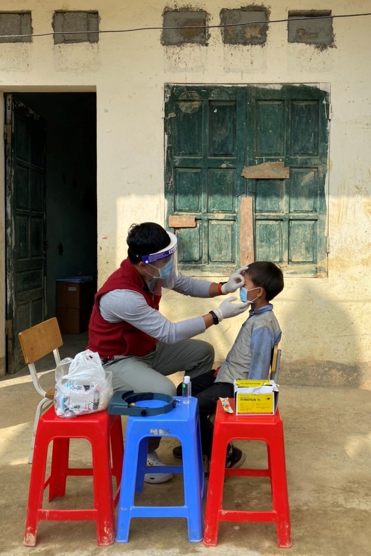 During routine survey in Viet Nam, a trachoma grader in examines the eyelid of a child for signs of trachoma. Grader wears a face shield, mask, and gloves as additional safety precautions during the COVID-19 pandemic