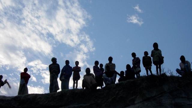 Backlit image of people standing on a hill with sky